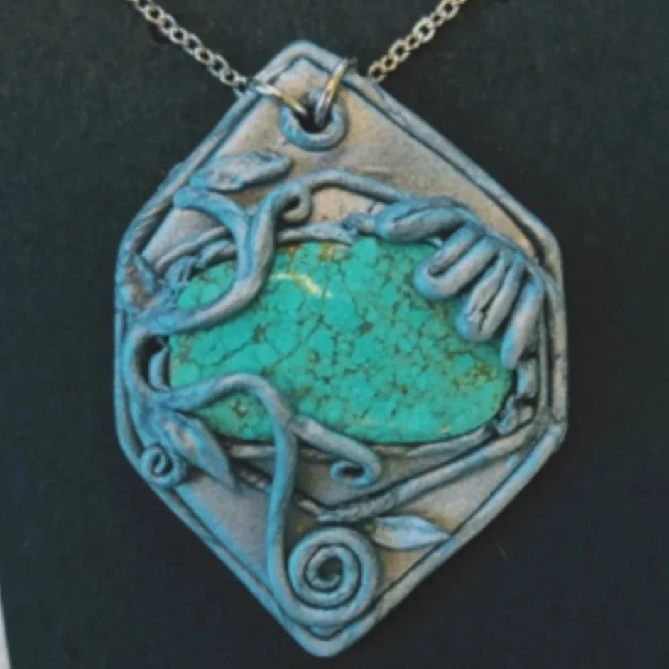 Silver necklace with a pendant featuring a turquoise stone wrapped in intricate silver vine-like designs.