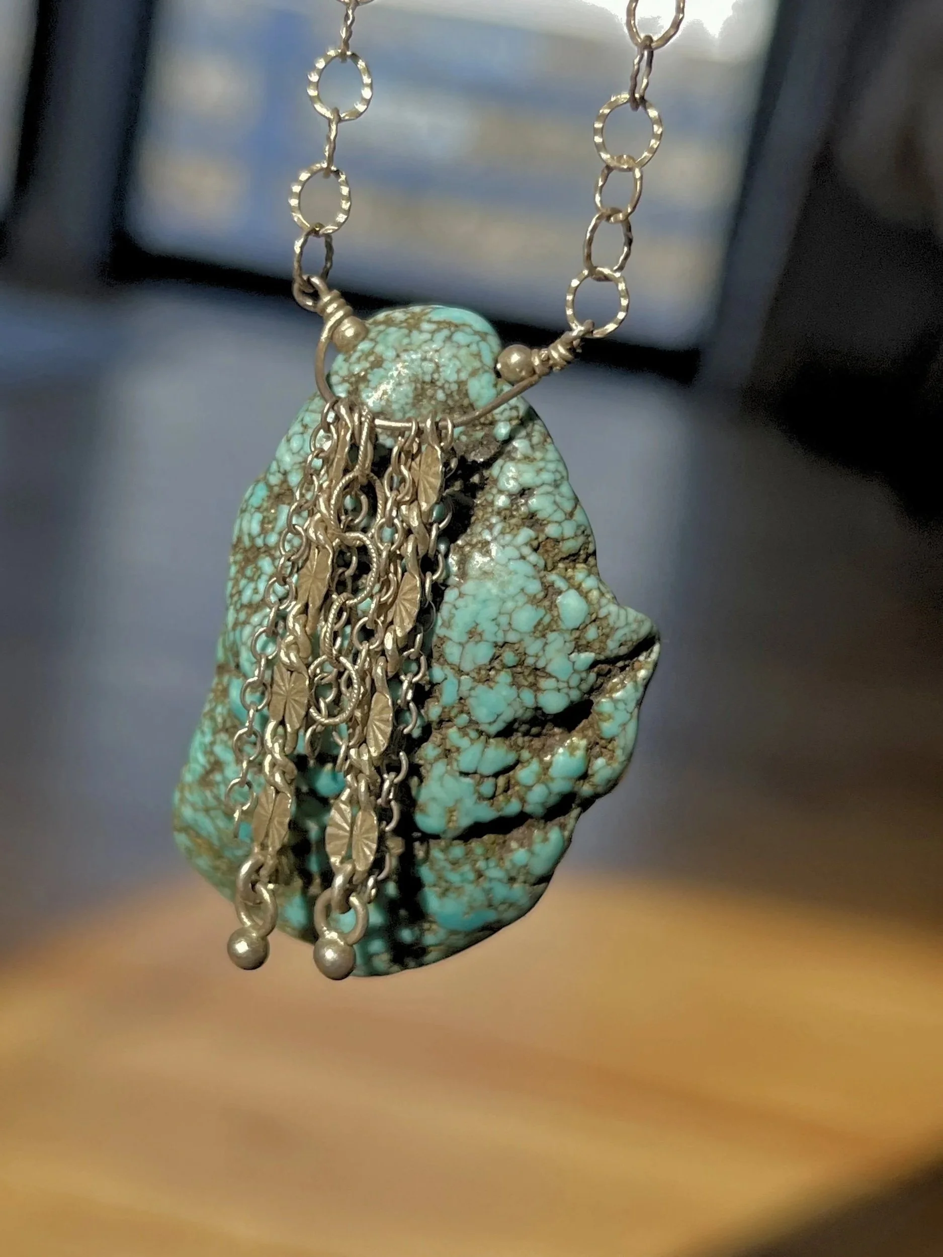 A pendant necklace with a turquoise stone and silver chains hanging from it.