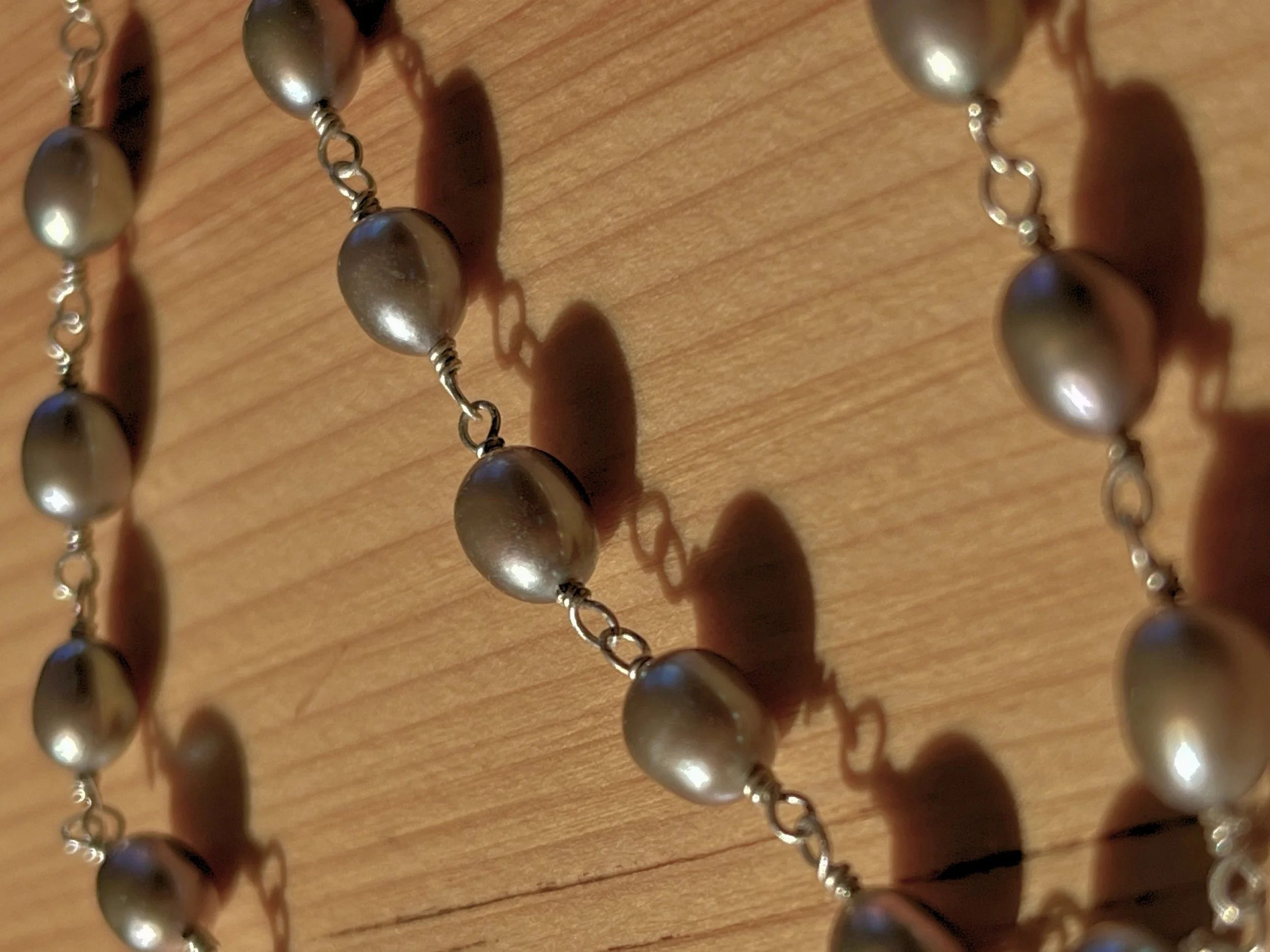 Close-up of a pearl necklace with silver links on a wooden surface, casting shadows.
