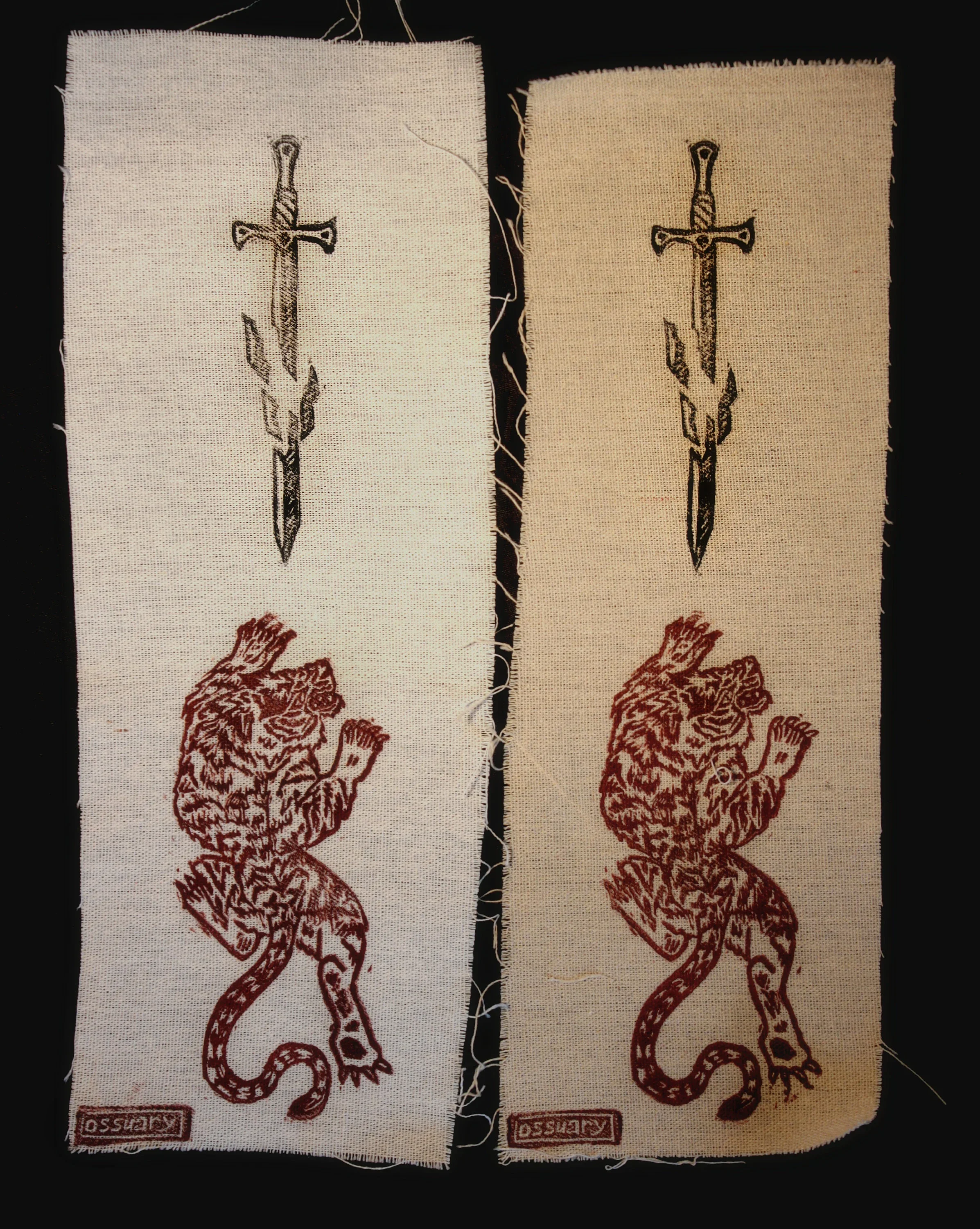 Two fabric patches with an embroidered design of a dagger above a lion with a raised paw, and a small rectangular label with text at the bottom.