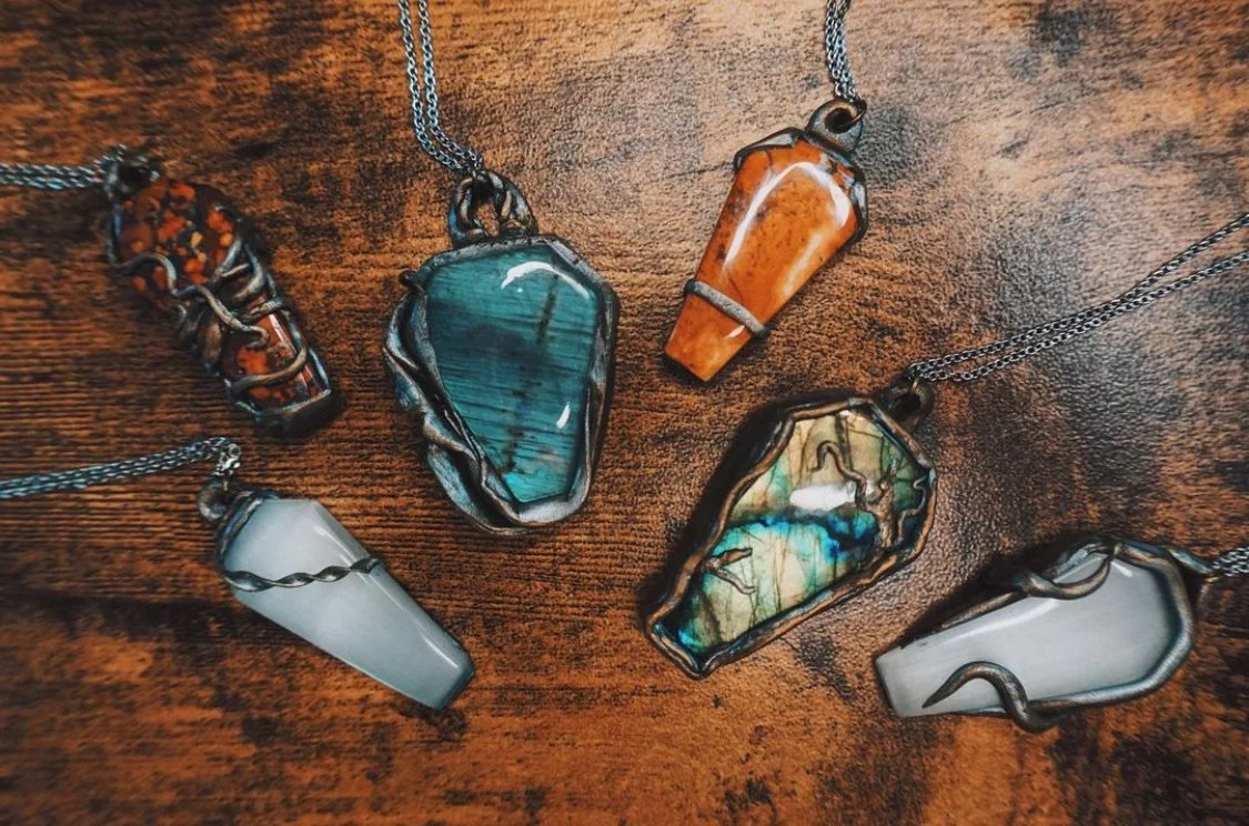 Six necklaces with various large, colorful gemstone pendants on a wooden surface.