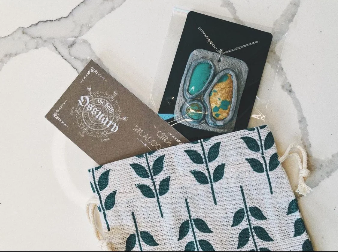A drawstring bag with a leafy pattern contains jewelry and business cards on a white marble surface.
