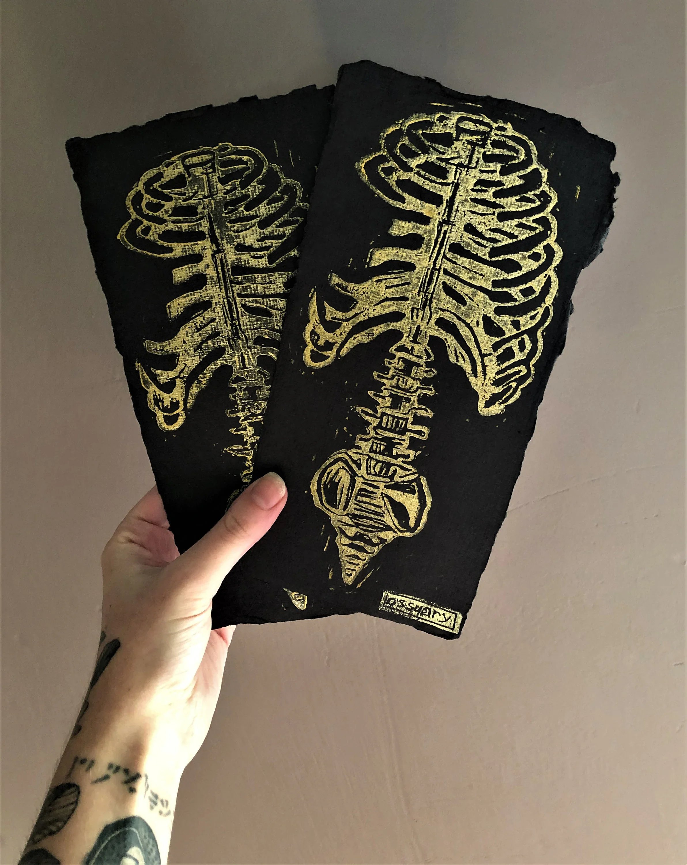 Two black cloths with a yellow skeleton print being held up against a beige wall.