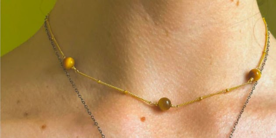 Close-up of a person wearing two delicate necklaces with small yellow beads.