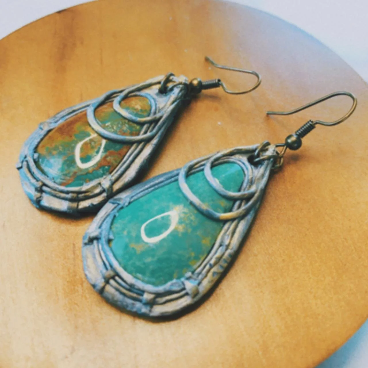Pair of turquoise and multicolored stone earrings with silver wire wrapping, resting on a wooden surface.