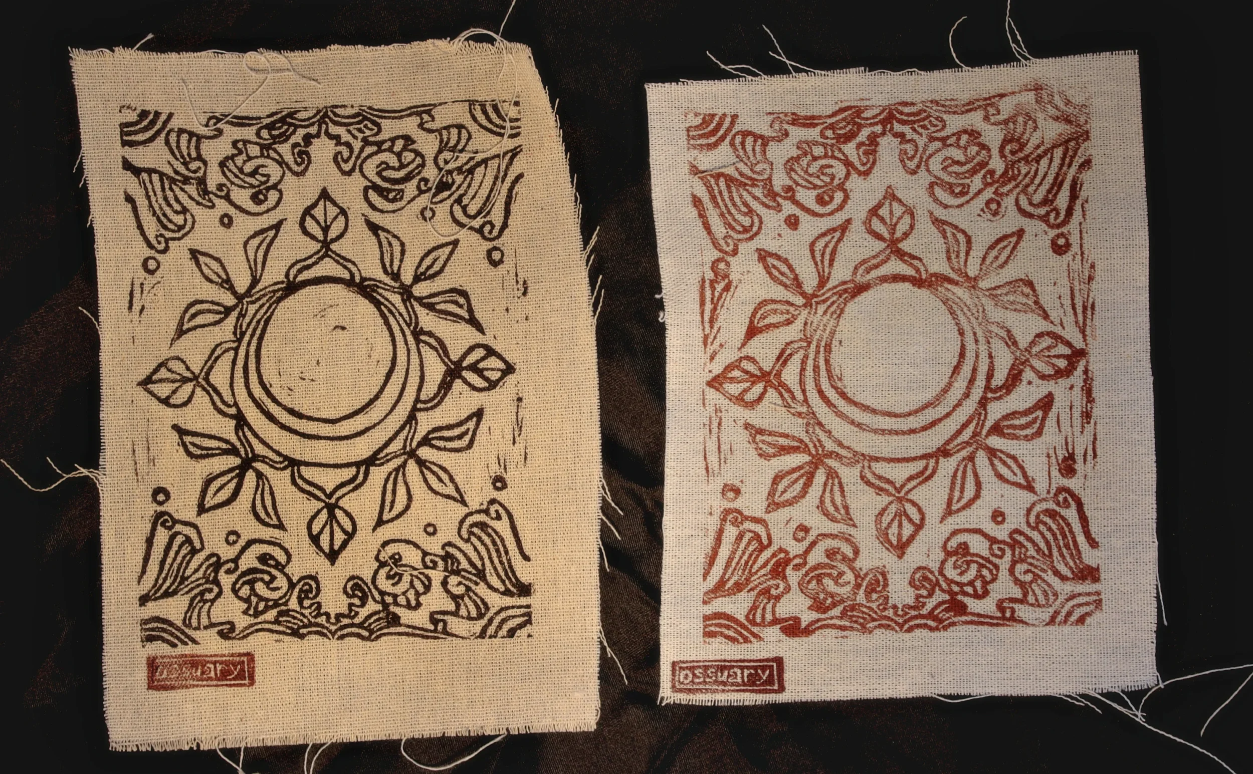 Two pieces of fabric with intricate floral and geometric patterns, one in dark ink on cream fabric and the other in red ink on white fabric, both with Chinese characters in red stamps at the bottom.