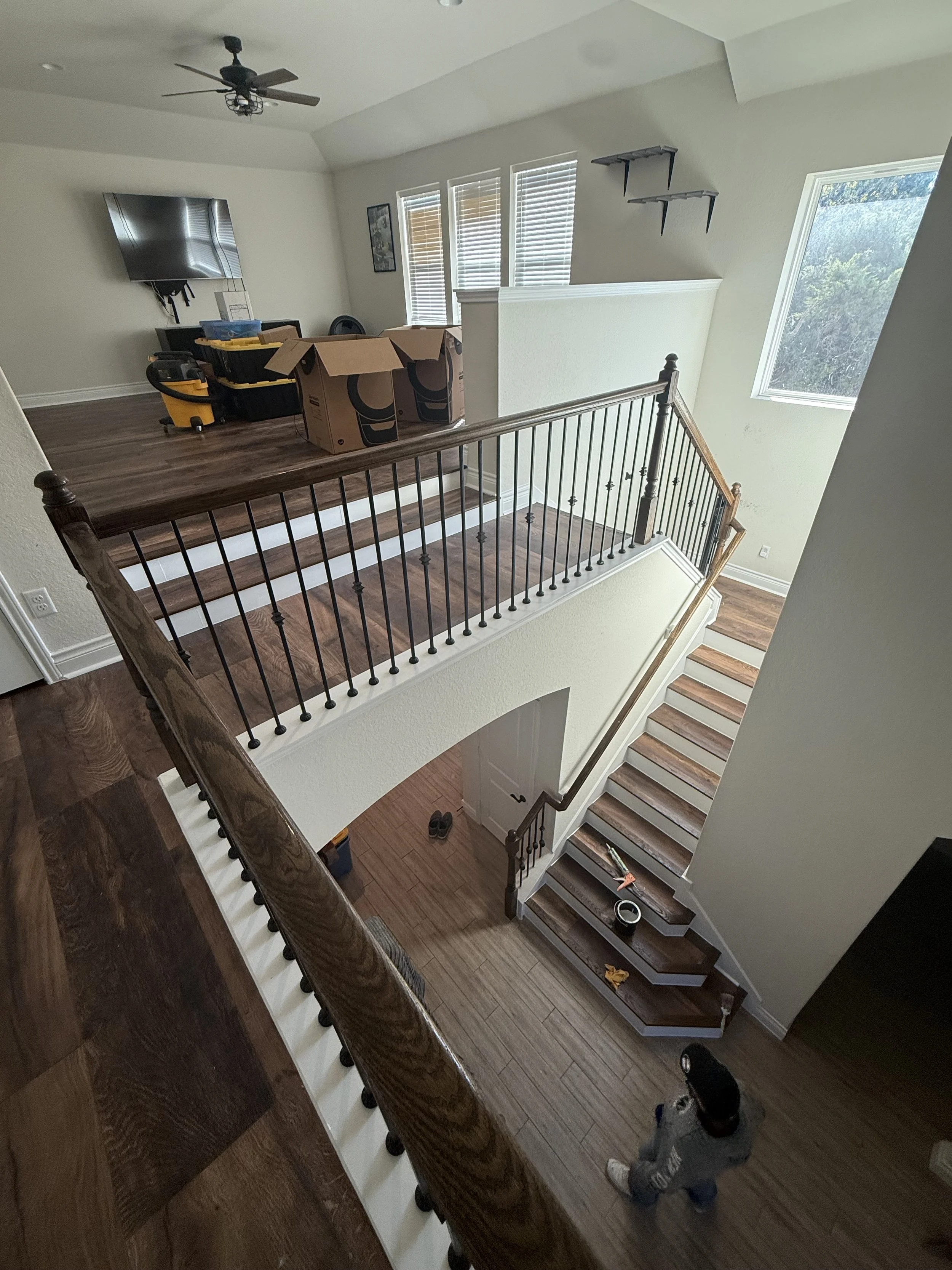 Interior of a multi-story home with a staircase, railing, and open living area. Moving boxes, a woman, and various items are visible.