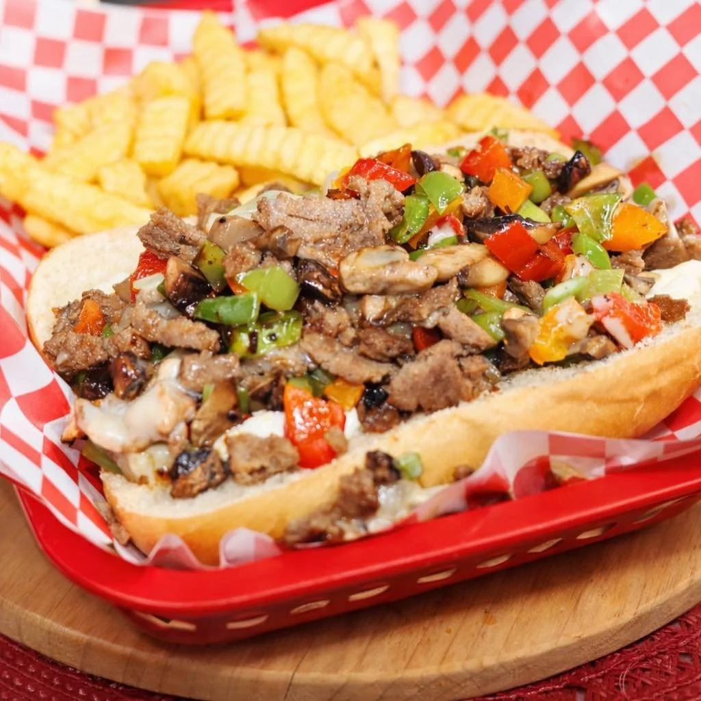Philly cheesesteak sandwich with fries in a red basket lined with checkered paper.