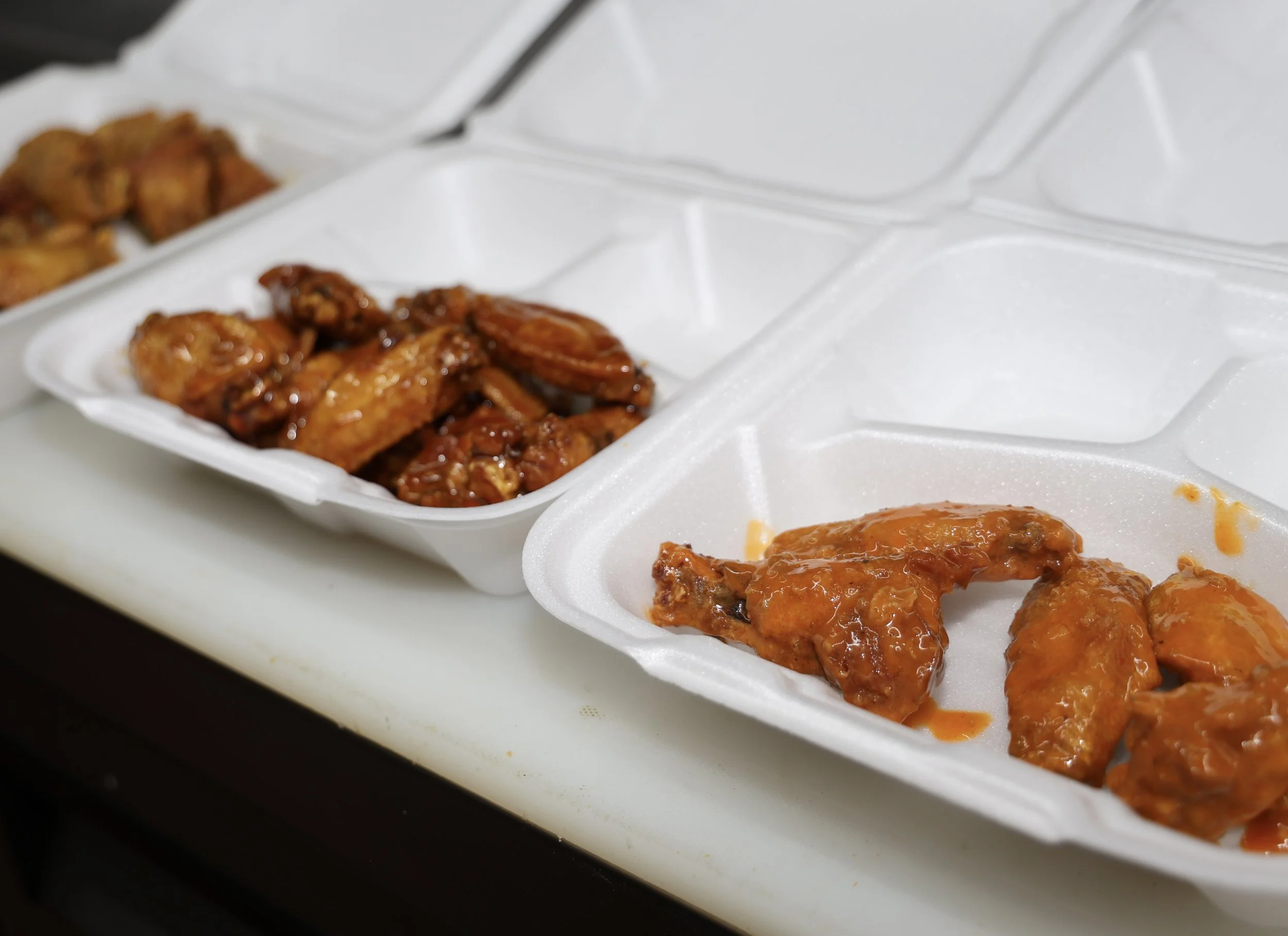 Takeout containers with glazed chicken wings and other fried chicken pieces.