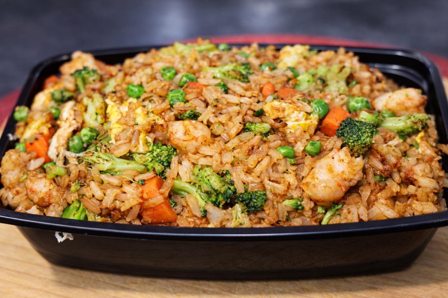 Container of fried rice with vegetables and shrimp.