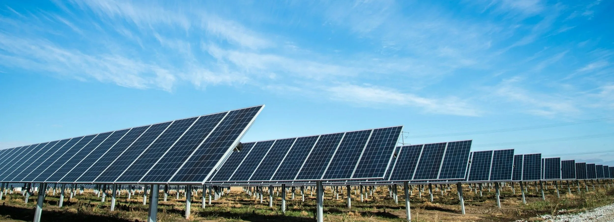 A large solar panel installation in a field under a blue sky with wispy clouds.
