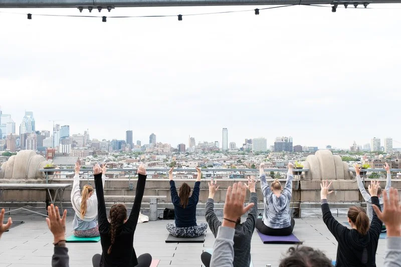 People participating in outdoor yoga session on rooftop with city skyline in the background.