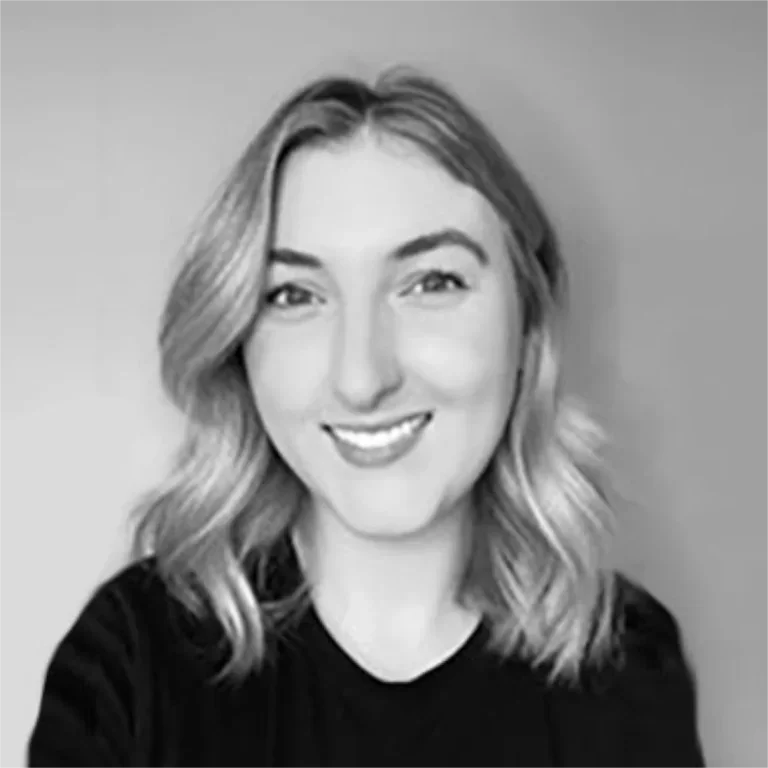 A smiling woman with shoulder-length wavy hair taking a selfie in front of a plain background.