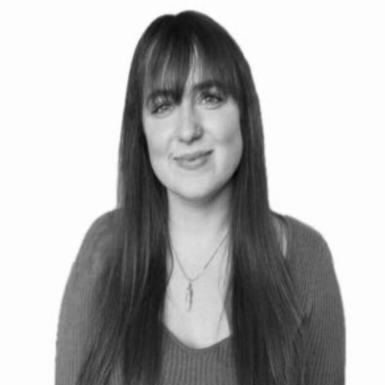 Black and white portrait of a woman with long dark hair and bangs, smiling softly, wearing a necklace and a sweater.