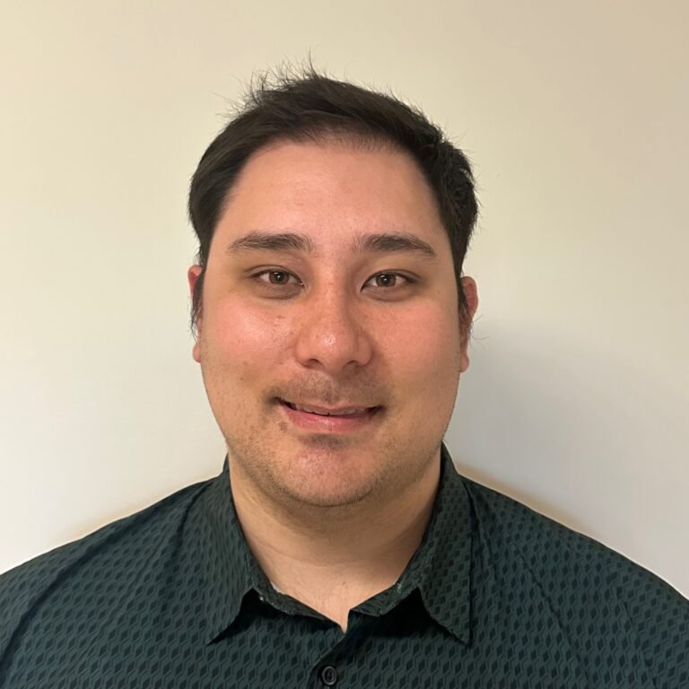 A young man with short black hair, light skin, wearing a black button-up shirt, smiling at the camera against a plain white background.