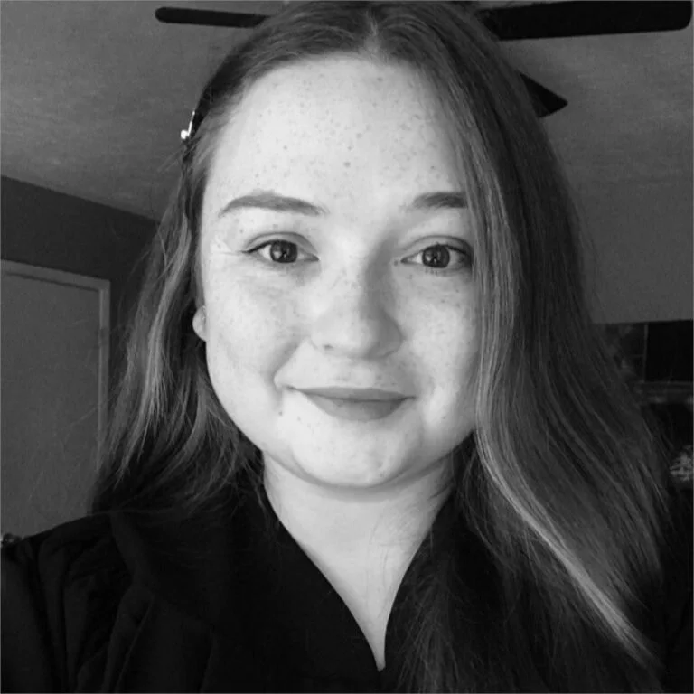 Black and white photo of a smiling young woman with long, wavy hair and freckles.