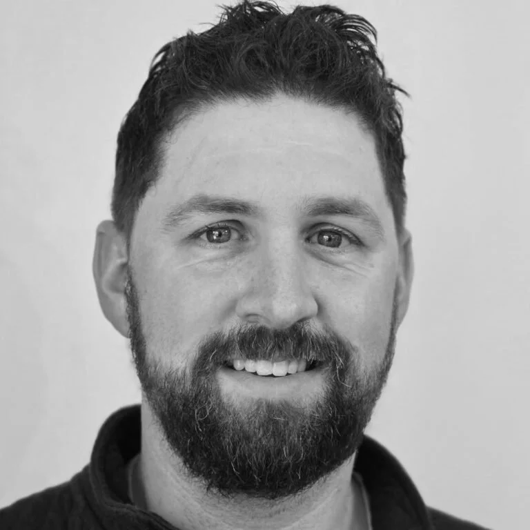 Black and white portrait of a man with short dark hair and a beard, smiling at the camera.