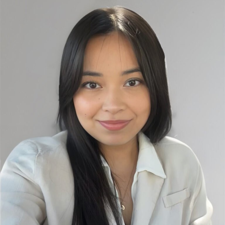 A young woman with straight black hair and light skin, smiling at the camera, wearing a light-colored blouse.