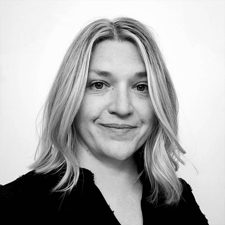 Black and white portrait of a woman with shoulder-length wavy hair, smiling lightly, wearing a dark top, against a plain background.