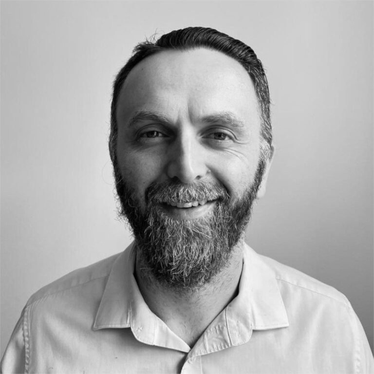 Black and white portrait of a man with a beard and short hair, smiling and wearing a collared shirt.