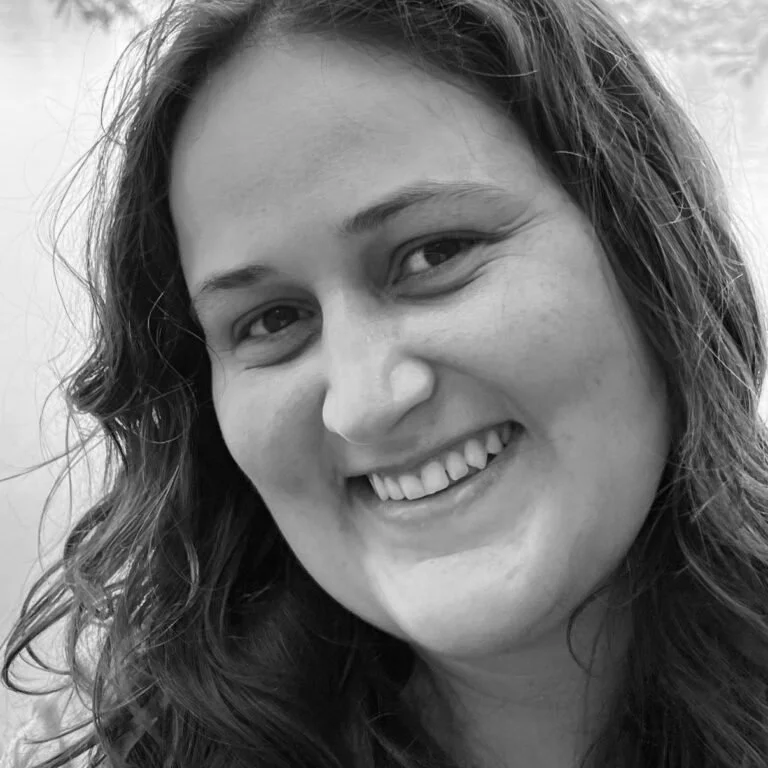 Close-up black and white photo of a woman smiling, with long wavy hair and visible teeth.