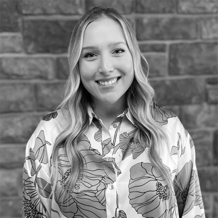 A young woman with long wavy hair smiling, standing against a brick wall.