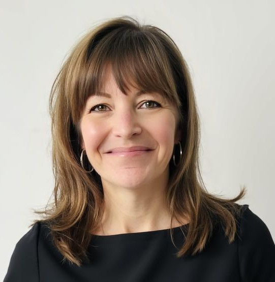 A woman with shoulder-length brown hair, wearing hoop earrings and a black top, smiling at the camera against a plain white background.