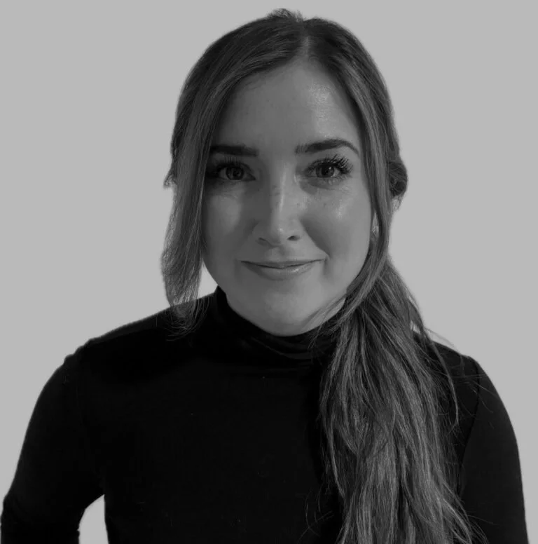 A woman with long hair wearing a black turtleneck, smiling at the camera, against a plain background.