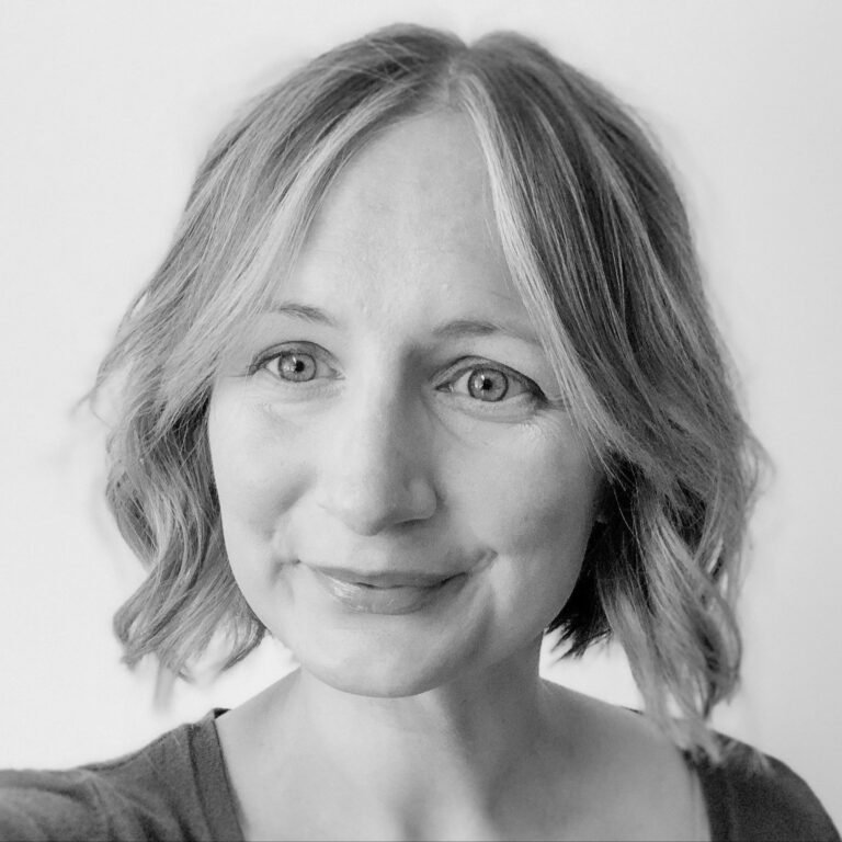 Black and white portrait of a woman with wavy, shoulder-length hair and light-colored eyes, smiling softly.