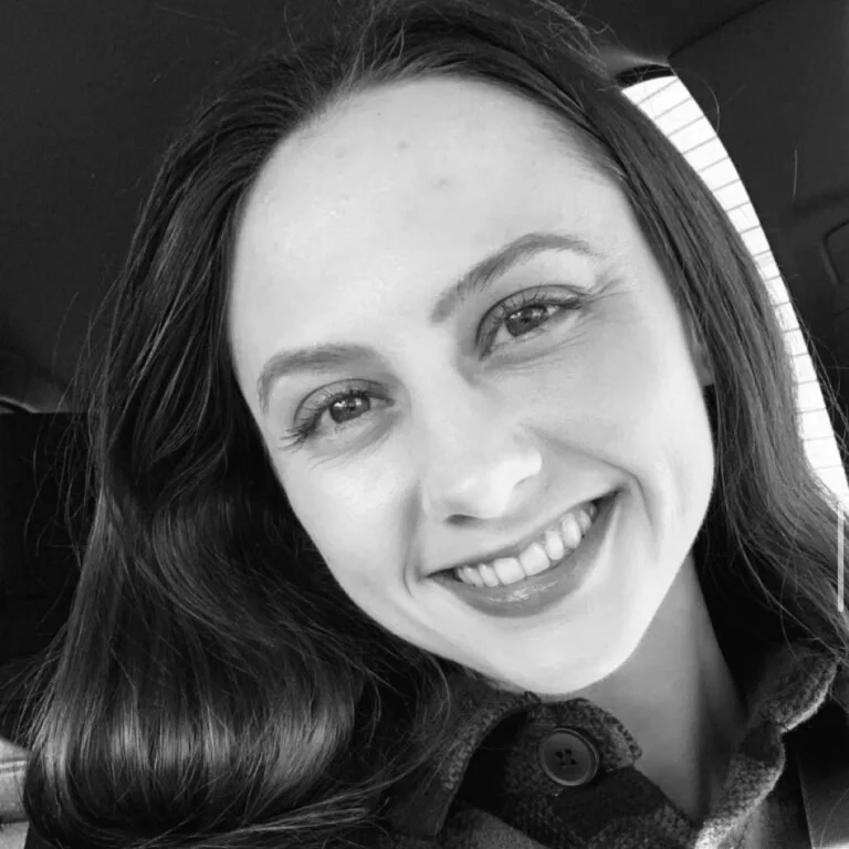 A black-and-white photo of a young woman smiling, with long hair, in a vehicle.