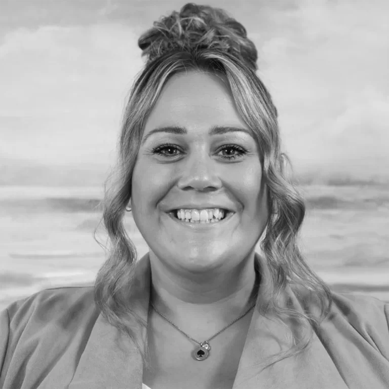 Black and white portrait of a smiling woman with wavy hair, wearing a necklace and a blazer.