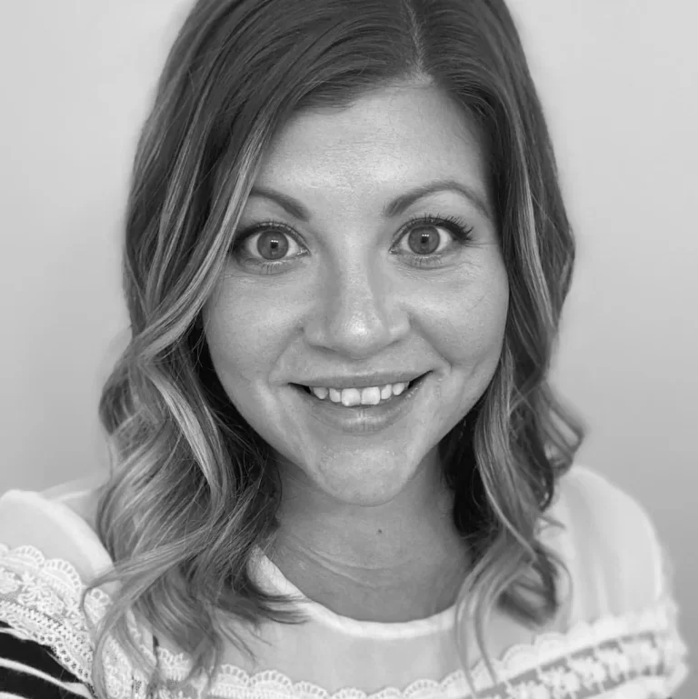 Black and white photo of a smiling woman with wavy hair wearing a blouse with lace details.