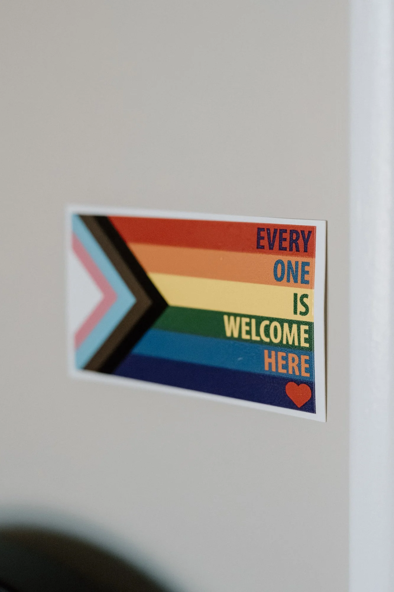 Colorful sticker with a chevron arrow and rainbow stripes that reads, "Every one is welcome here" with a small heart symbol.