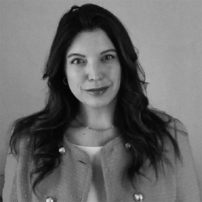 Black and white portrait of a woman with long wavy hair, wearing earrings and a necklace, smiling softly at the camera.