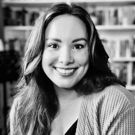 Black and white photo of a smiling woman with long wavy hair, in front of a bookshelf.