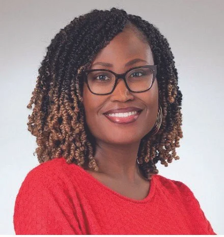 A woman with shoulder-length curly hair wearing glasses and a red sweater, smiling against a neutral background.