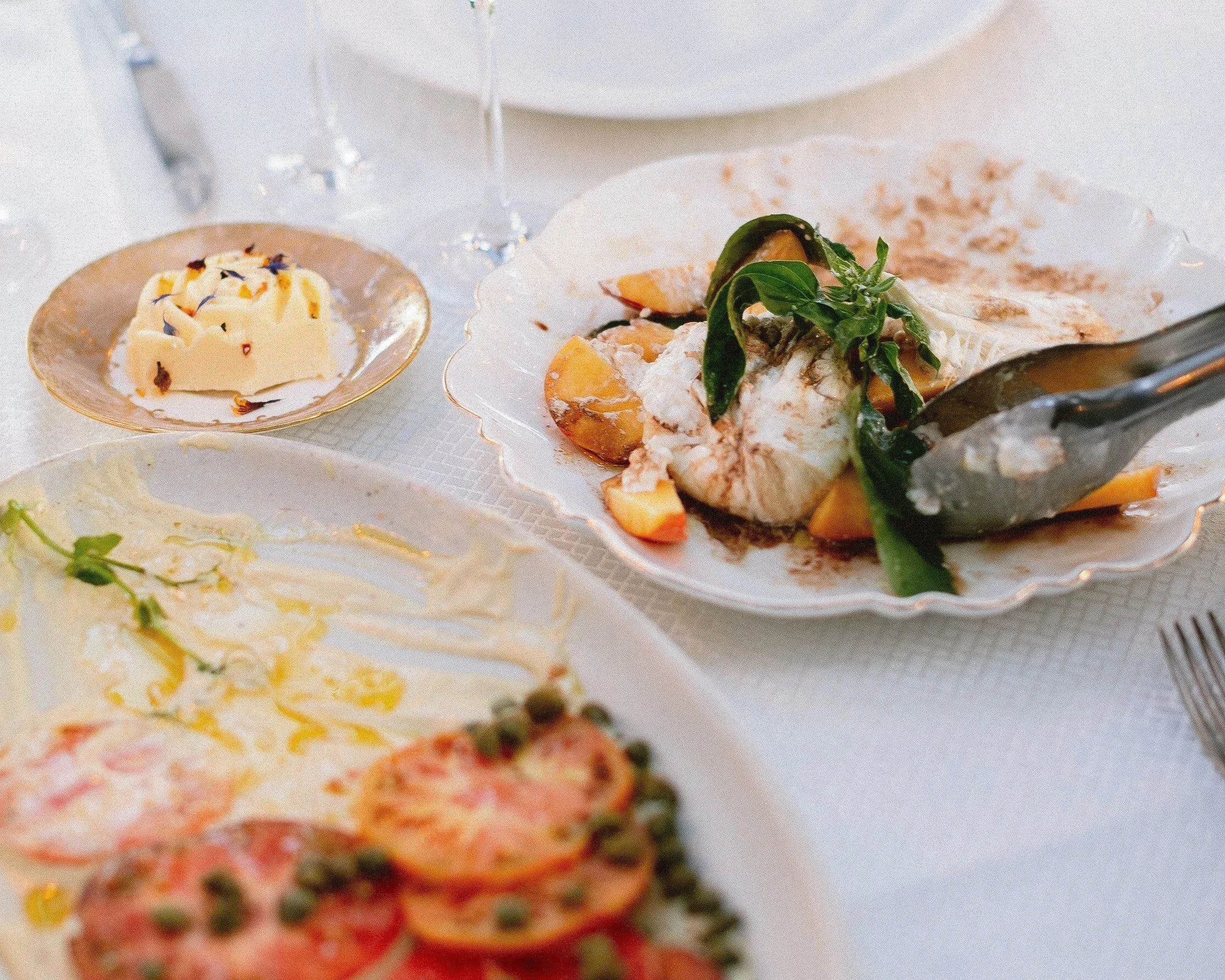 Elegant table setting with a seafood dish, a small plate of cheese, and a partially eaten plate of salad with tomatoes, peas, and greens.