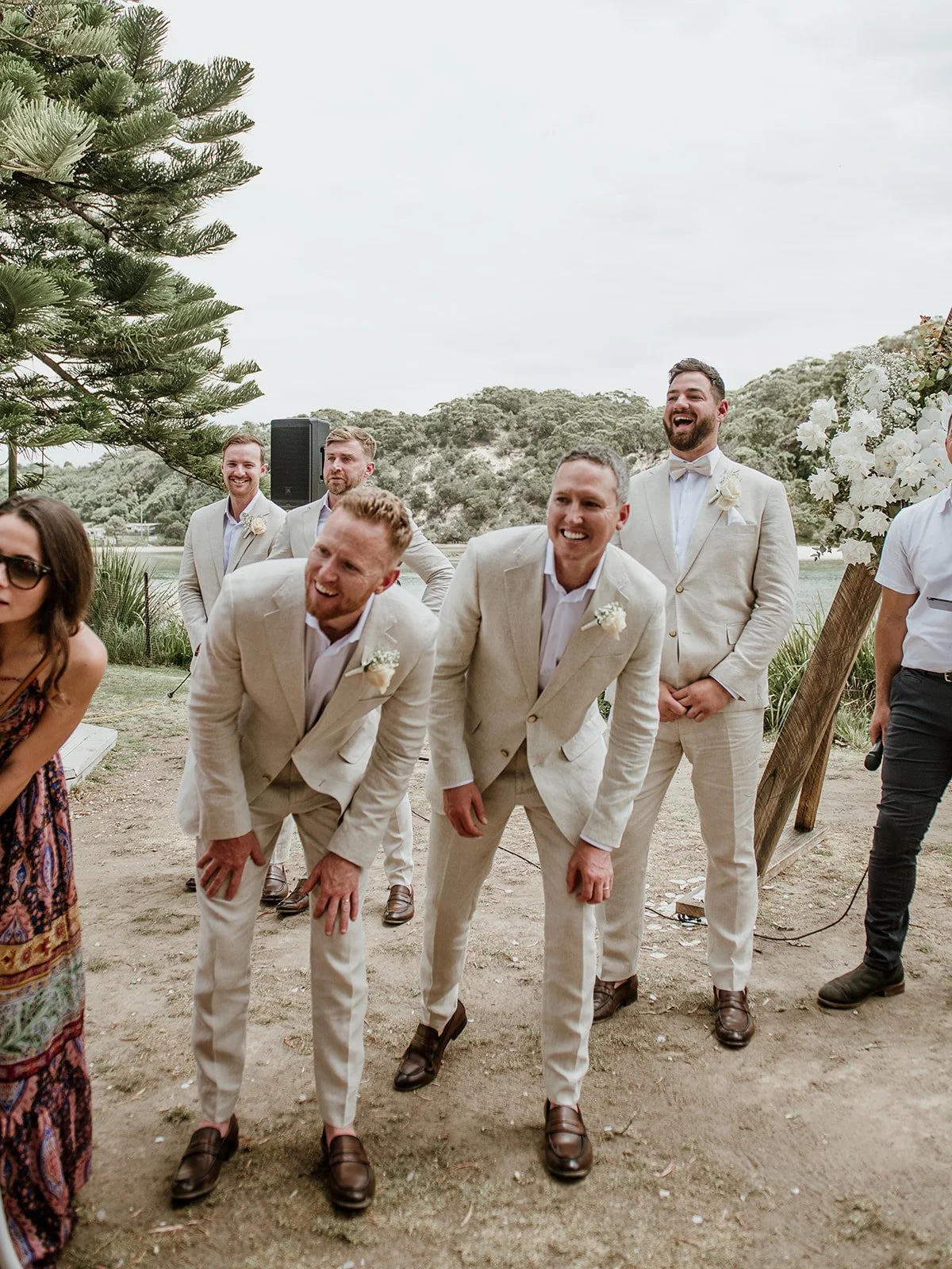 Groomsmen in beige suits laughing at outdoor wedding ceremony.