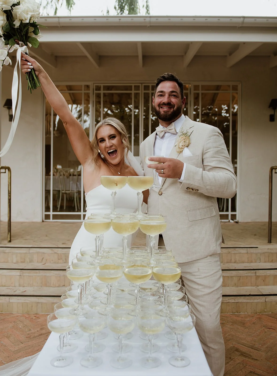 Happy bride and groom with champagne glasses on a tiered table, celebrating at a wedding reception.