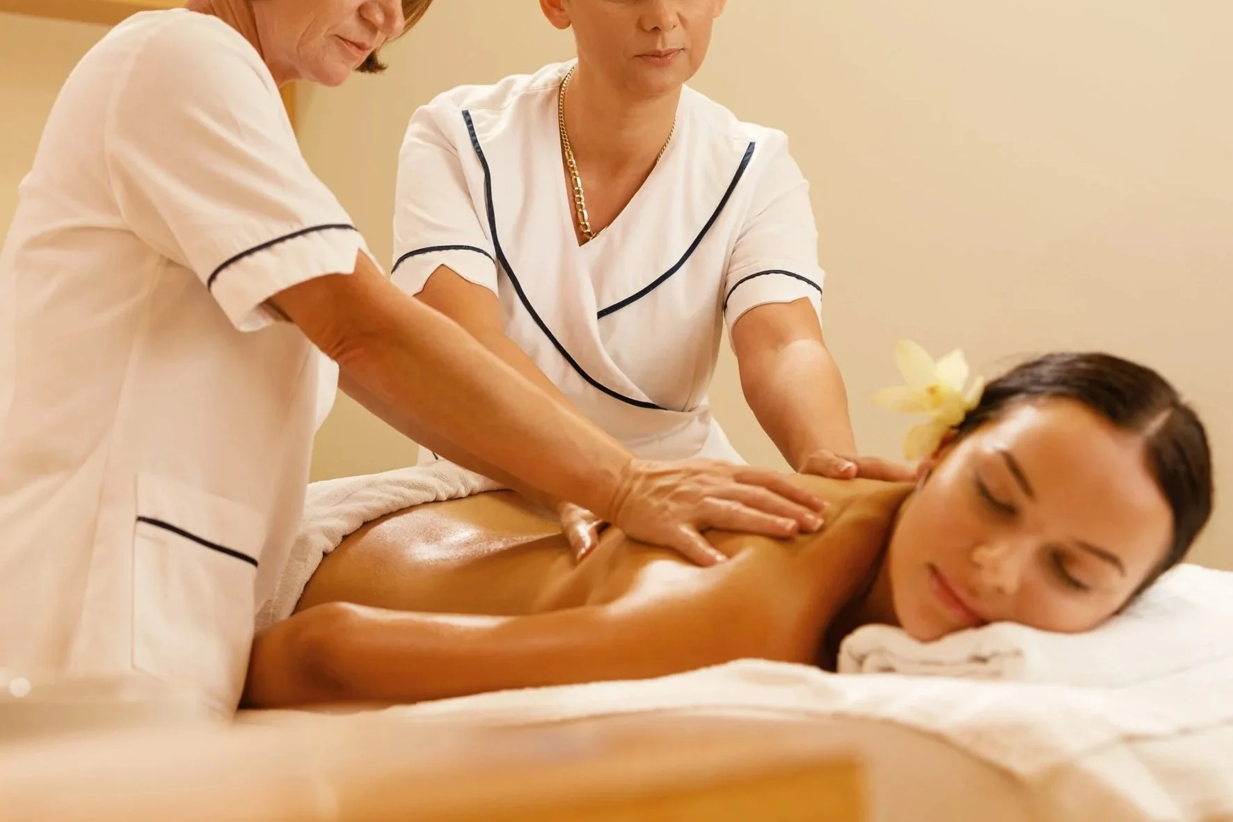 A woman receiving a massage from a massage therapist in a spa setting, with a flower in her hair and a serene expression on her face.