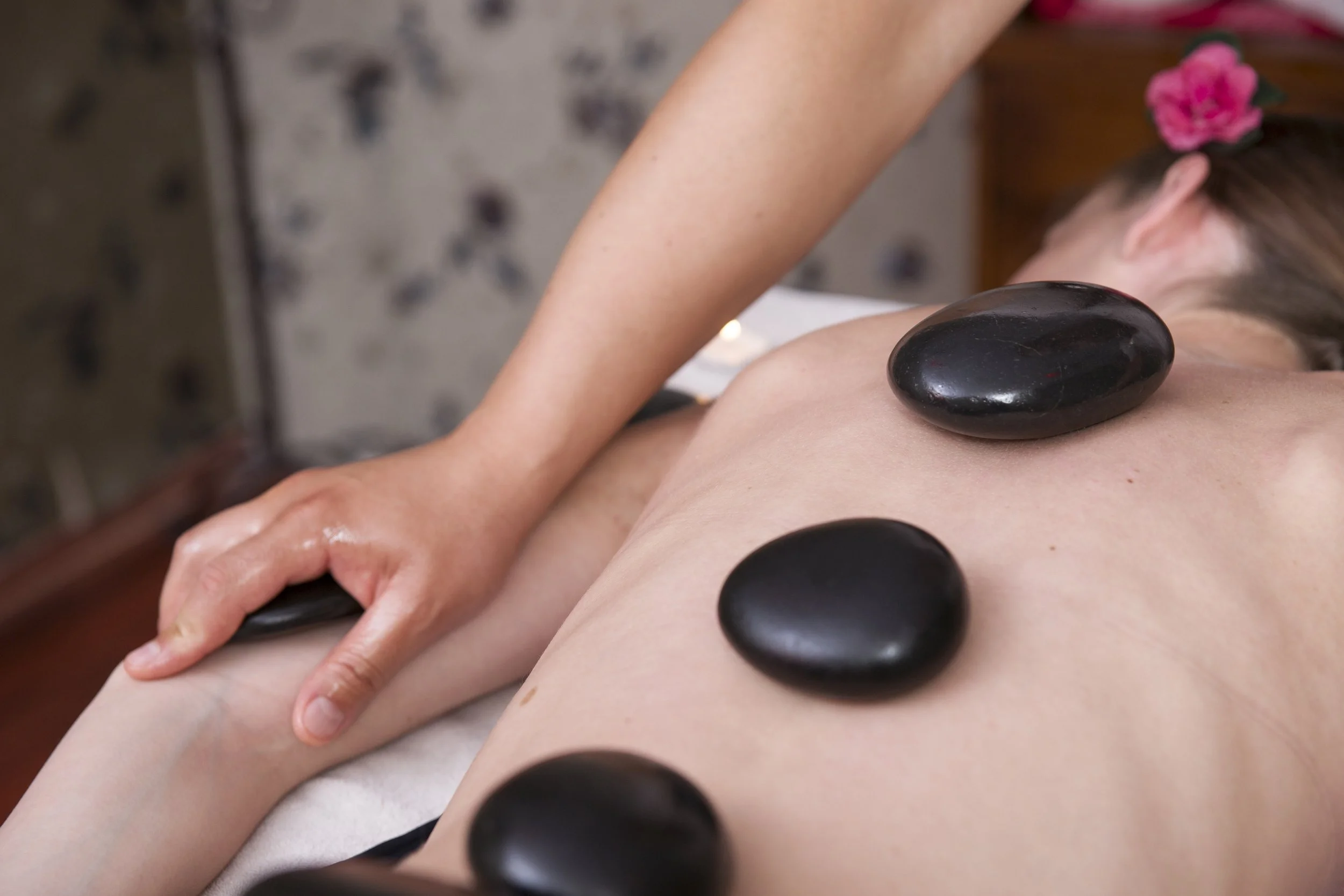 Person receiving hot stone massage on back with black stones