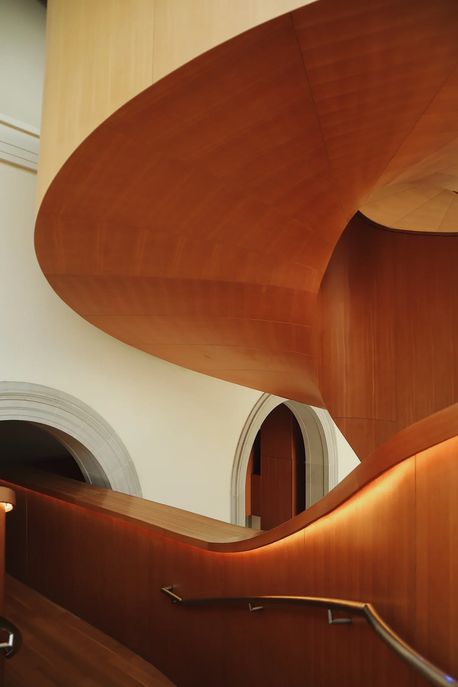 Escalier intérieur en bois courbé dans un bâtiment calme avec murs en pierre blanche et arches.