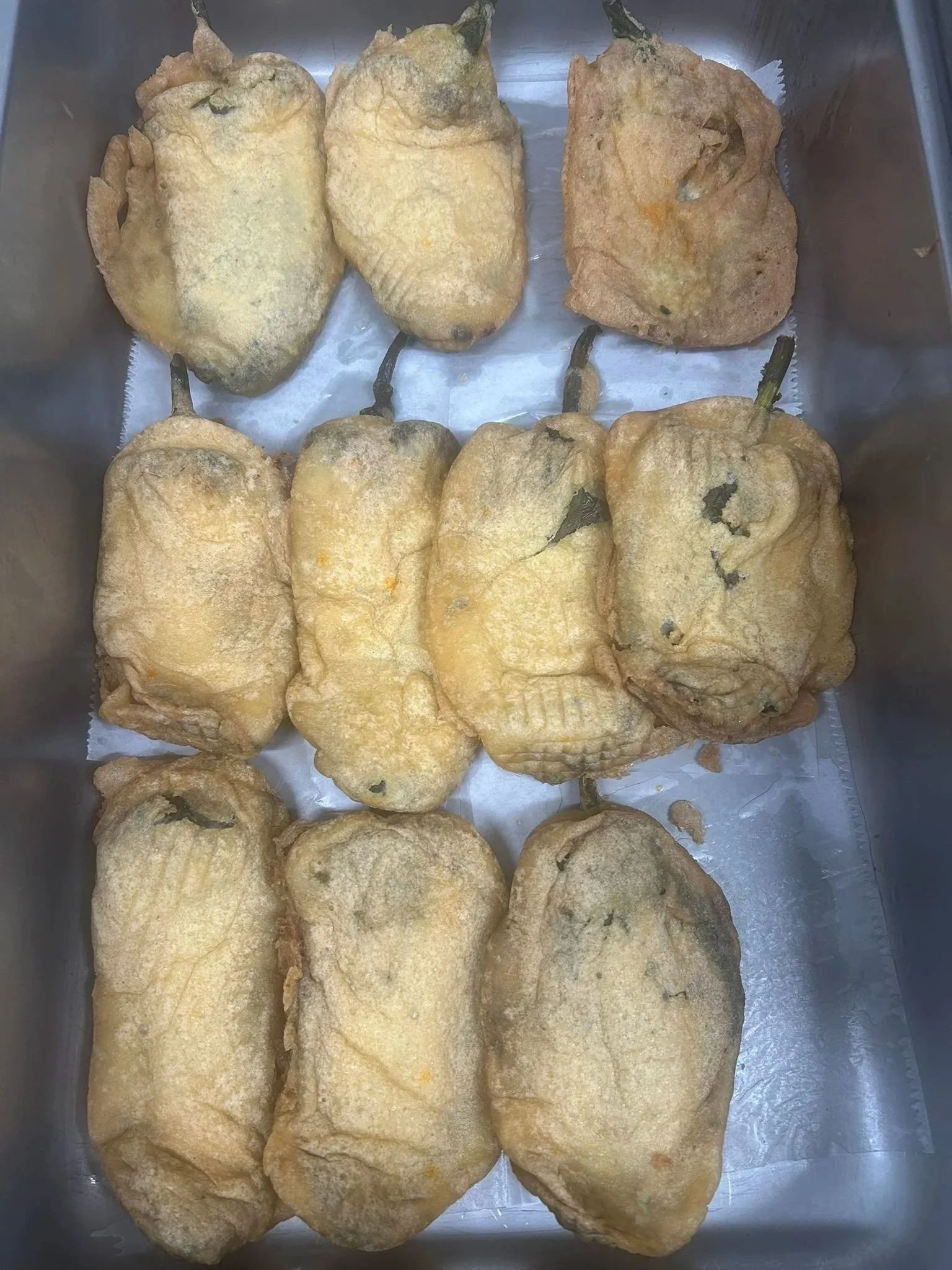 Fried stuffed peppers in a tray, with some showing the stem and others without.