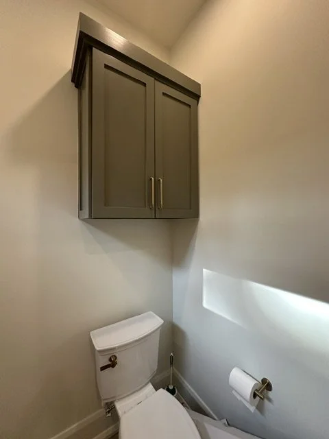 Gray wall-mounted bathroom cabinet above a white toilet with a closed lid, and a toilet paper holder on the wall.