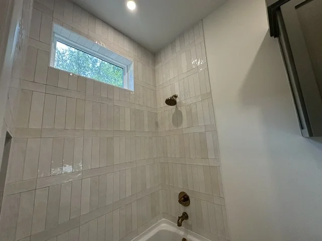 Bathroom shower with white subway tiles, small rectangular window, and a brass showerhead and faucet.