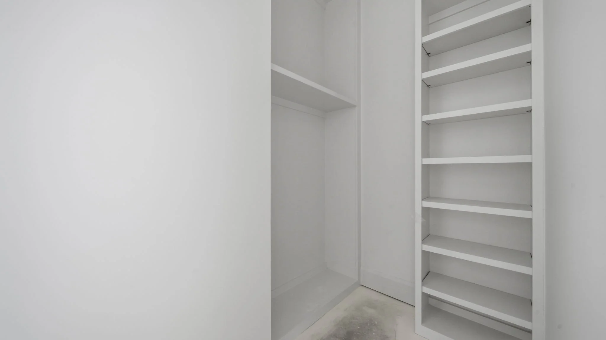 Empty white closet with built-in shelves on the right side.