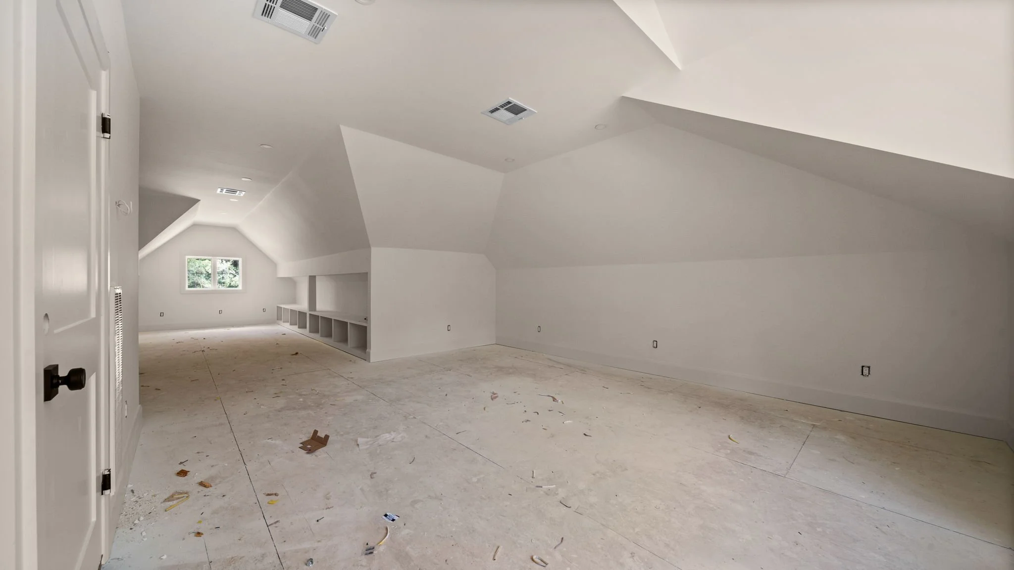 Empty attic room with white walls and sloped ceiling, window, built-in shelves, and scattered debris on the floor.