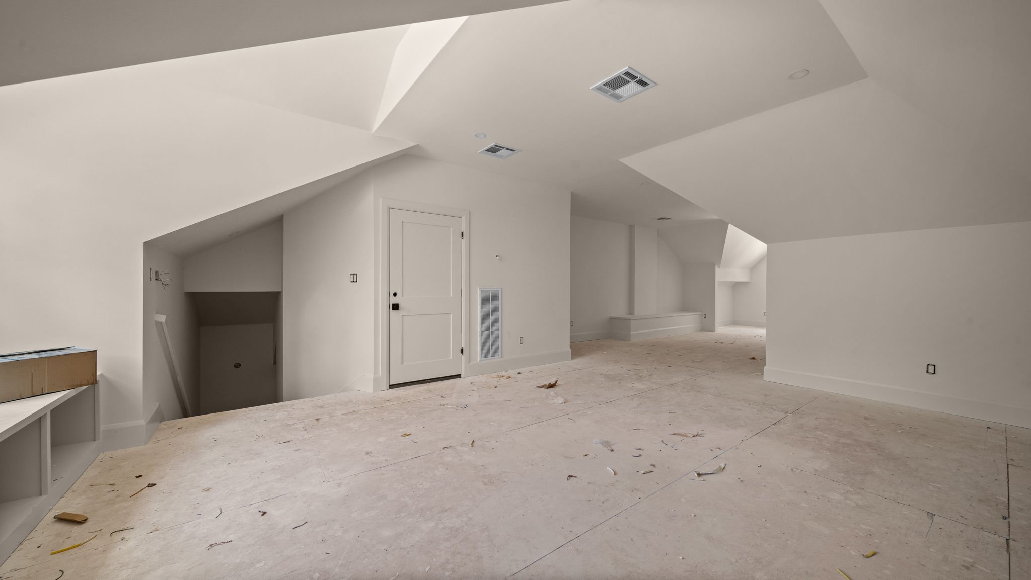 Empty room with sloped ceilings, white walls, unfinished flooring, and built-in shelves, likely under construction or renovation.