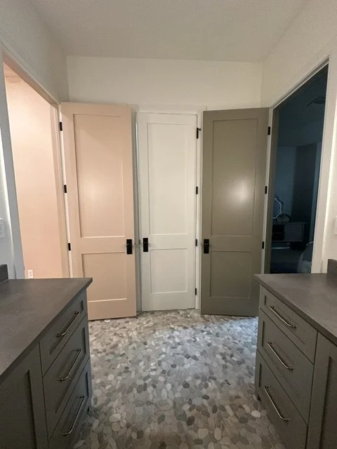View of a laundry room with four closed cabinet doors, two beige and two gray, on a wall with patterned tile flooring, and gray countertops on either side.
