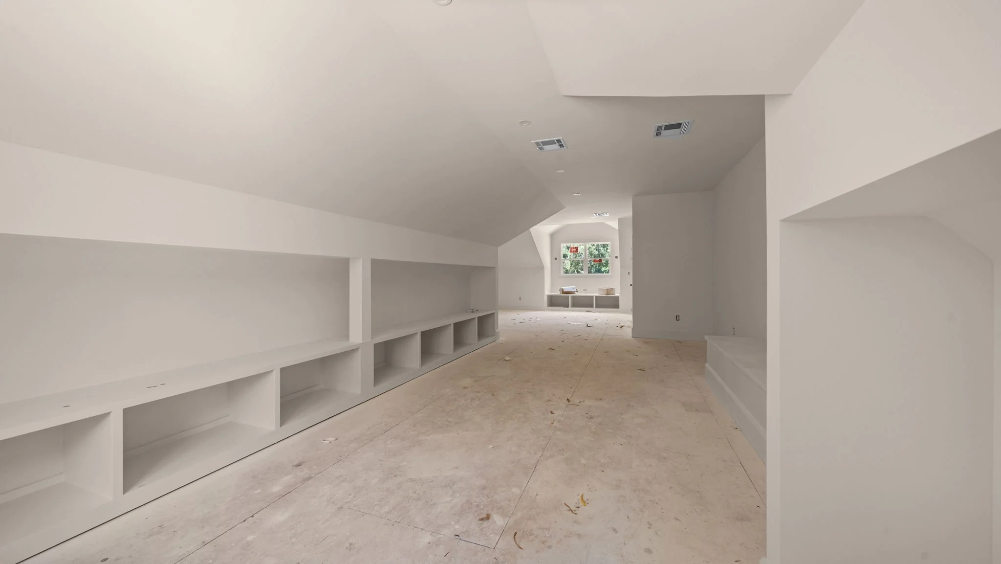 Interior of a new, unfinished house with white walls, built-in shelves, and a window at the far end.